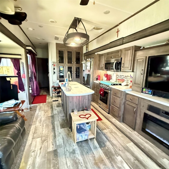 kitchen featuring visible vents, an island with sink, light wood-type flooring, light countertops, and stainless steel appliances