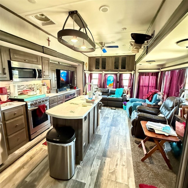 kitchen with light wood finished floors, a center island, open floor plan, light countertops, and appliances with stainless steel finishes