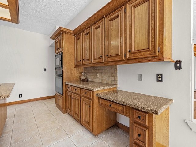 kitchen featuring light tile patterned floors, decorative backsplash, brown cabinets, and black appliances