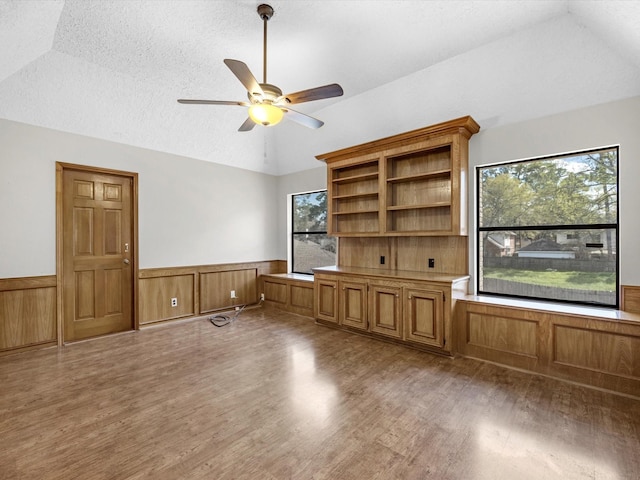 interior space featuring ceiling fan, lofted ceiling, wainscoting, light wood-style floors, and a textured ceiling