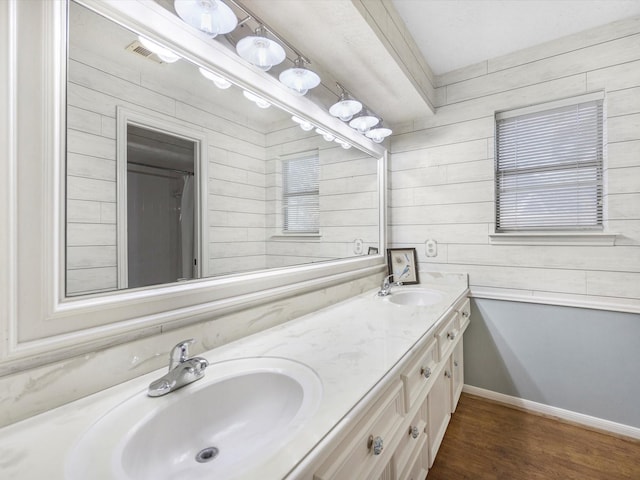 bathroom featuring double vanity, wood finished floors, baseboards, and a sink