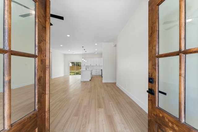 hall with recessed lighting, baseboards, light wood finished floors, and a sink