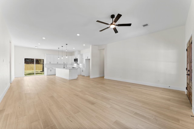 unfurnished living room featuring ceiling fan, light wood-style flooring, visible vents, and a sink