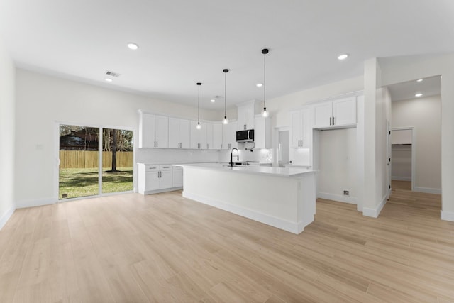 kitchen featuring stainless steel microwave, visible vents, an island with sink, light wood-type flooring, and light countertops