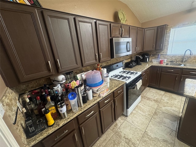 kitchen featuring a sink, vaulted ceiling, dark brown cabinetry, gas range, and stainless steel microwave