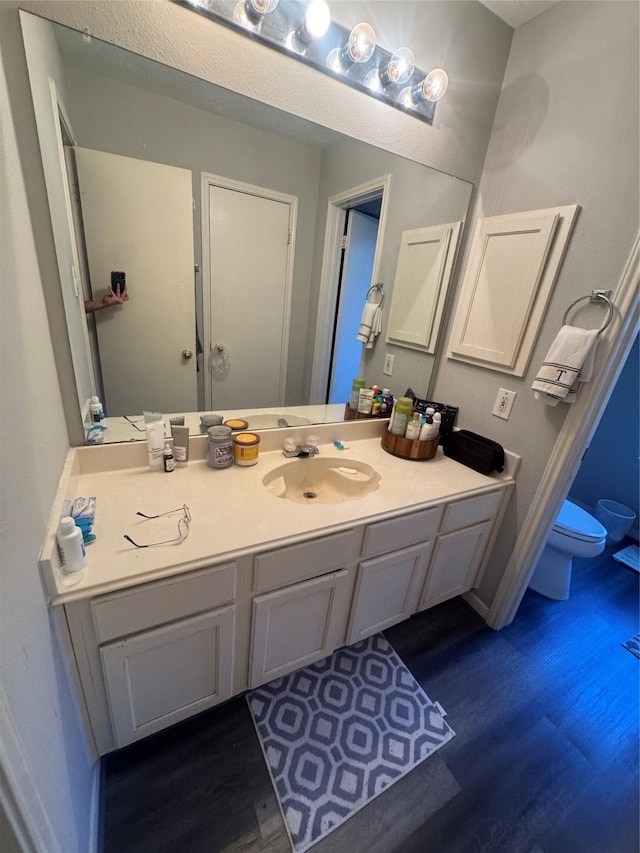 bathroom with toilet, vanity, baseboards, and wood finished floors