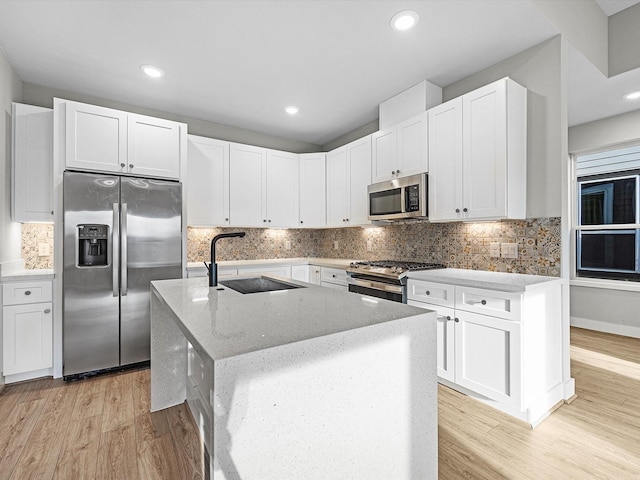 kitchen featuring light wood finished floors, light stone countertops, stainless steel appliances, white cabinetry, and a sink