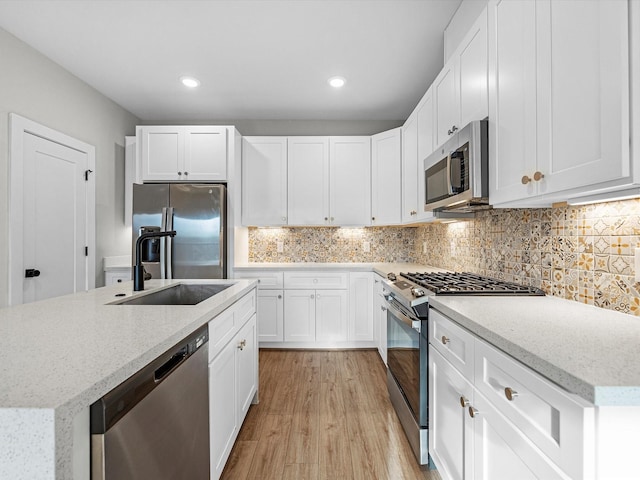 kitchen featuring backsplash, light wood-style floors, white cabinets, stainless steel appliances, and a sink