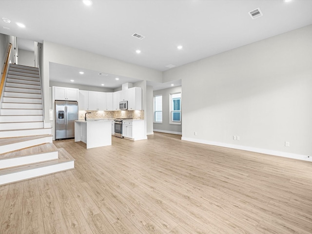 unfurnished living room featuring stairs, recessed lighting, light wood-style floors, and visible vents