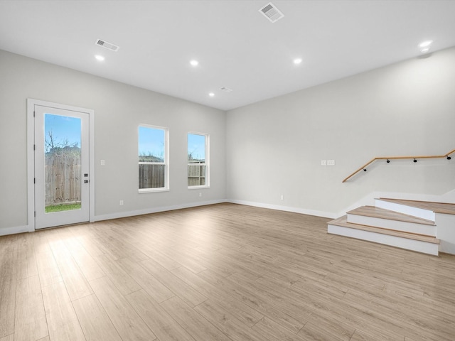 unfurnished living room featuring visible vents, plenty of natural light, light wood-style flooring, and stairs