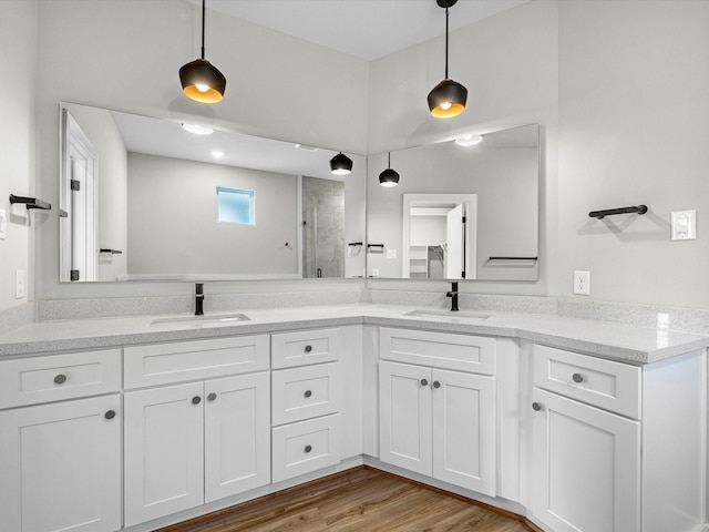 bathroom featuring double vanity, a shower stall, wood finished floors, and a sink