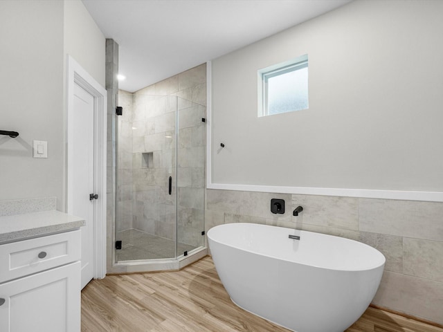 full bathroom with vanity, a stall shower, wood finished floors, a soaking tub, and tile walls