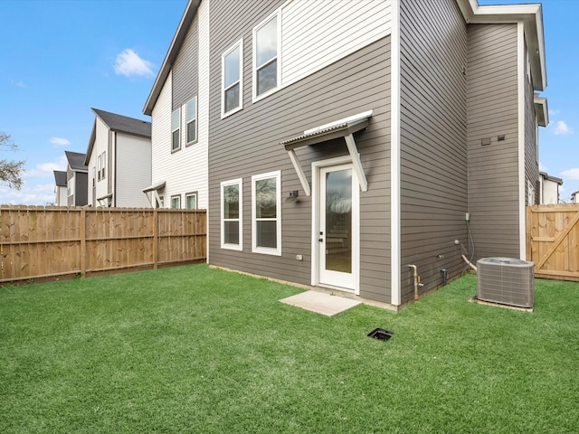 rear view of house featuring cooling unit, a lawn, and a fenced backyard