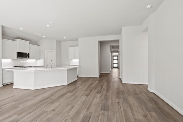 kitchen with stainless steel microwave, white cabinetry, light countertops, and light wood-style floors