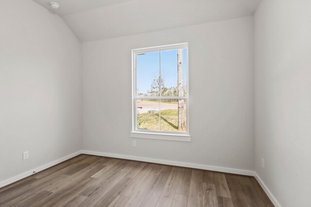 empty room featuring lofted ceiling, baseboards, and wood finished floors