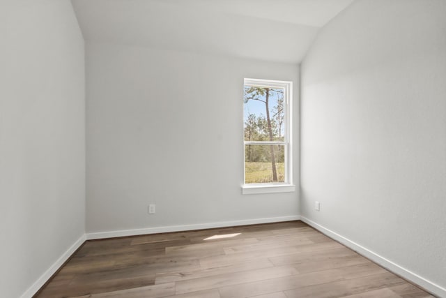 spare room featuring vaulted ceiling, light wood-style flooring, and baseboards