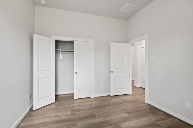 unfurnished bedroom with wood finished floors, visible vents, a closet, and baseboards