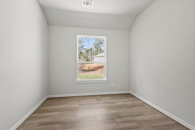 unfurnished room with light wood finished floors, visible vents, lofted ceiling, and baseboards