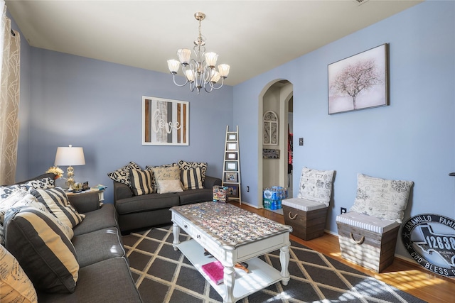 living area featuring arched walkways, a chandelier, baseboards, and wood finished floors