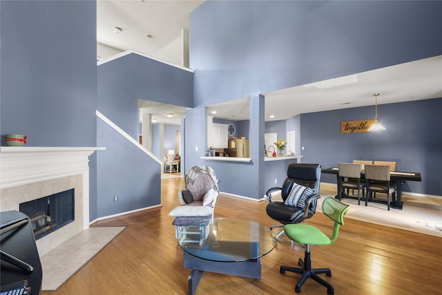 living room featuring hardwood / wood-style flooring, a high ceiling, a fireplace, and baseboards