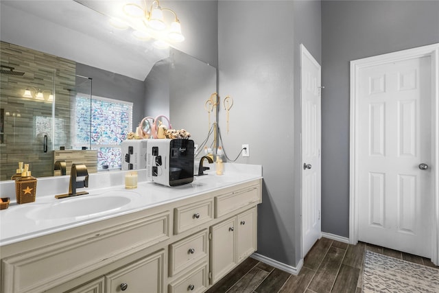 bathroom featuring wood finish floors, a sink, a shower stall, double vanity, and baseboards