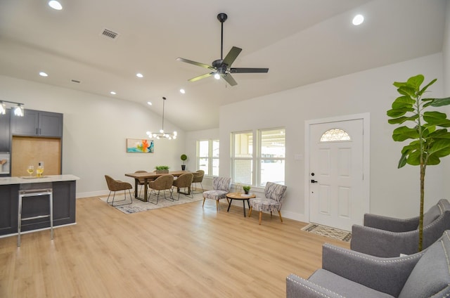 living room featuring vaulted ceiling, ceiling fan with notable chandelier, visible vents, and light wood-type flooring