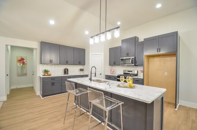 kitchen with light stone counters, light wood finished floors, gray cabinets, a sink, and appliances with stainless steel finishes