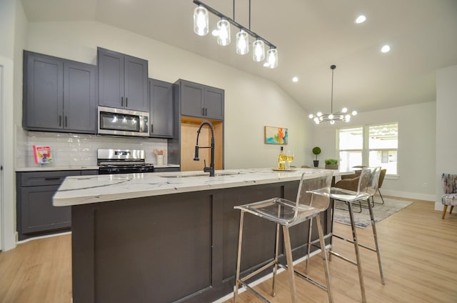 kitchen featuring vaulted ceiling, light stone counters, appliances with stainless steel finishes, and a sink