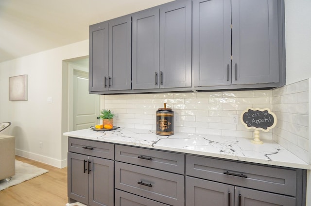 kitchen with light stone counters, baseboards, gray cabinetry, decorative backsplash, and light wood-style floors