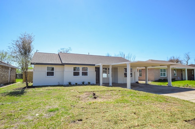 ranch-style house featuring roof with shingles, concrete driveway, a front yard, an attached carport, and brick siding