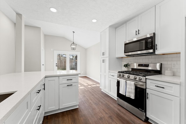 kitchen featuring stainless steel appliances, vaulted ceiling, dark wood-type flooring, white cabinetry, and backsplash