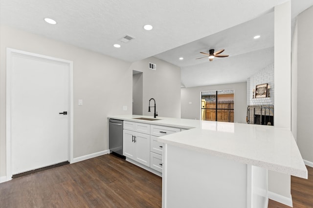 kitchen featuring dark wood-type flooring, stainless steel dishwasher, a peninsula, a brick fireplace, and ceiling fan