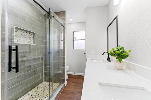 bathroom featuring toilet, a stall shower, wood finished floors, baseboards, and vanity