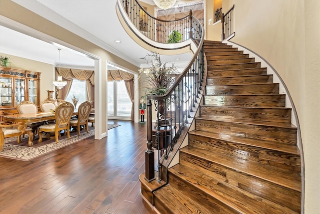 stairs with a notable chandelier, wood finished floors, a towering ceiling, and ornamental molding