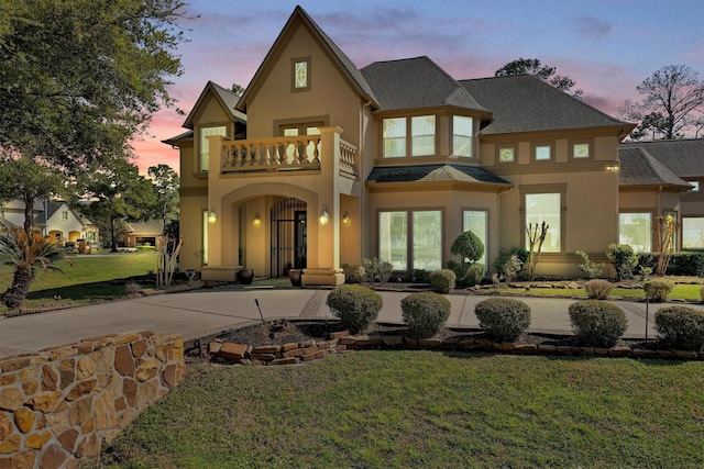 back of house featuring a shingled roof, a balcony, a yard, and stucco siding