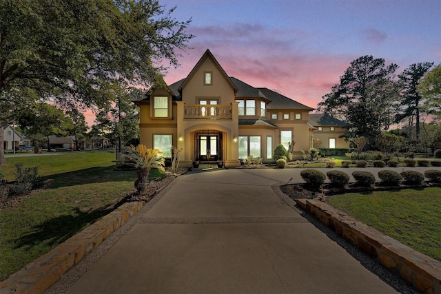 view of front of home with curved driveway, a front lawn, stucco siding, french doors, and a balcony