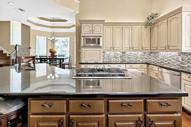 kitchen featuring a kitchen island, decorative backsplash, appliances with stainless steel finishes, an inviting chandelier, and a raised ceiling