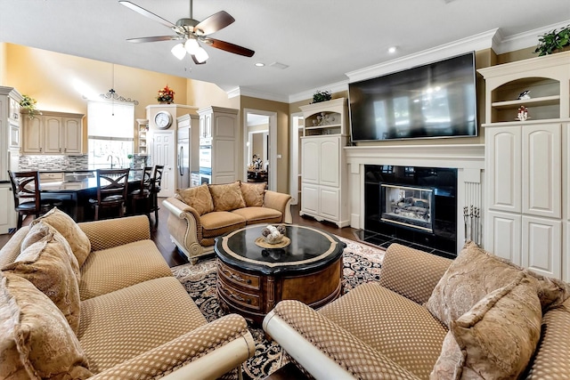 living area with dark wood-style flooring, a fireplace with flush hearth, a ceiling fan, and ornamental molding