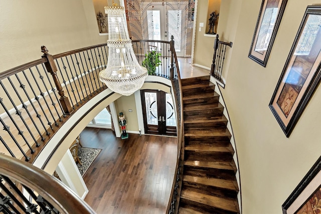 stairway with wood finished floors, french doors, arched walkways, a healthy amount of sunlight, and a chandelier