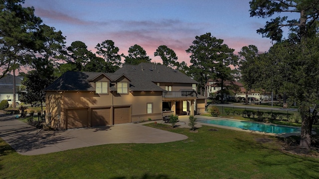 back of house with a fenced in pool, stucco siding, a balcony, a yard, and driveway