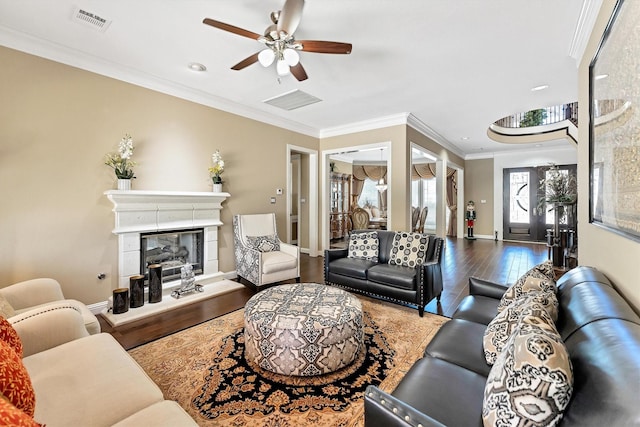 living area with wood finished floors, visible vents, ceiling fan, a glass covered fireplace, and crown molding