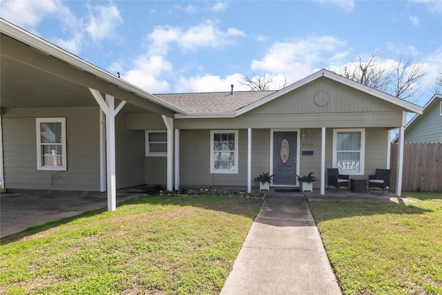 ranch-style home with covered porch, a shingled roof, a front lawn, and fence