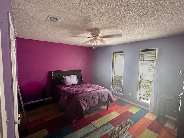 bedroom featuring visible vents, baseboards, a textured ceiling, and a ceiling fan