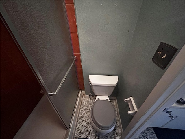 bathroom featuring tile patterned flooring, a shower stall, toilet, and a textured wall