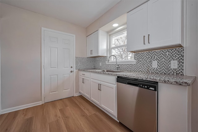 kitchen featuring light wood-type flooring, decorative backsplash, stainless steel dishwasher, white cabinets, and a sink