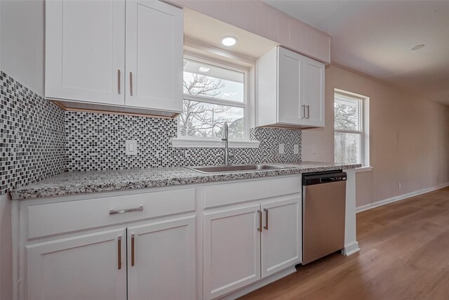 kitchen with a sink, stainless steel dishwasher, white cabinetry, light wood-style floors, and decorative backsplash