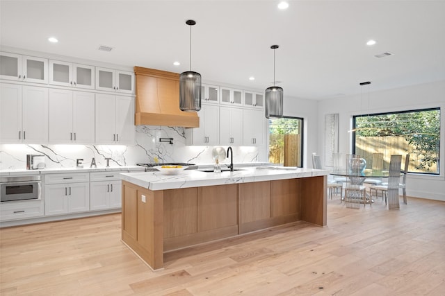 kitchen with oven, a center island with sink, a sink, decorative backsplash, and custom exhaust hood