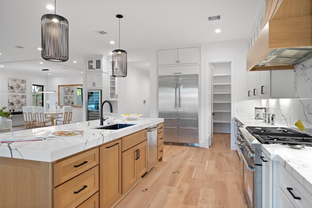 kitchen with premium range hood, light wood-type flooring, visible vents, a sink, and premium appliances