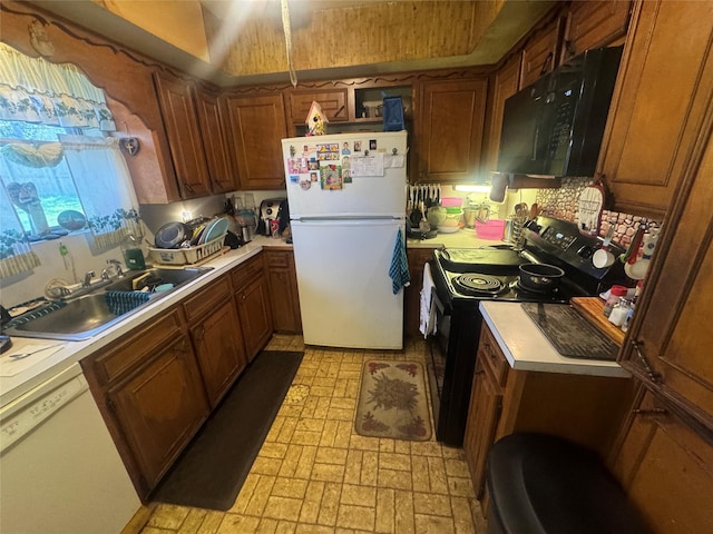 kitchen featuring brown cabinetry, black appliances, light countertops, and a sink