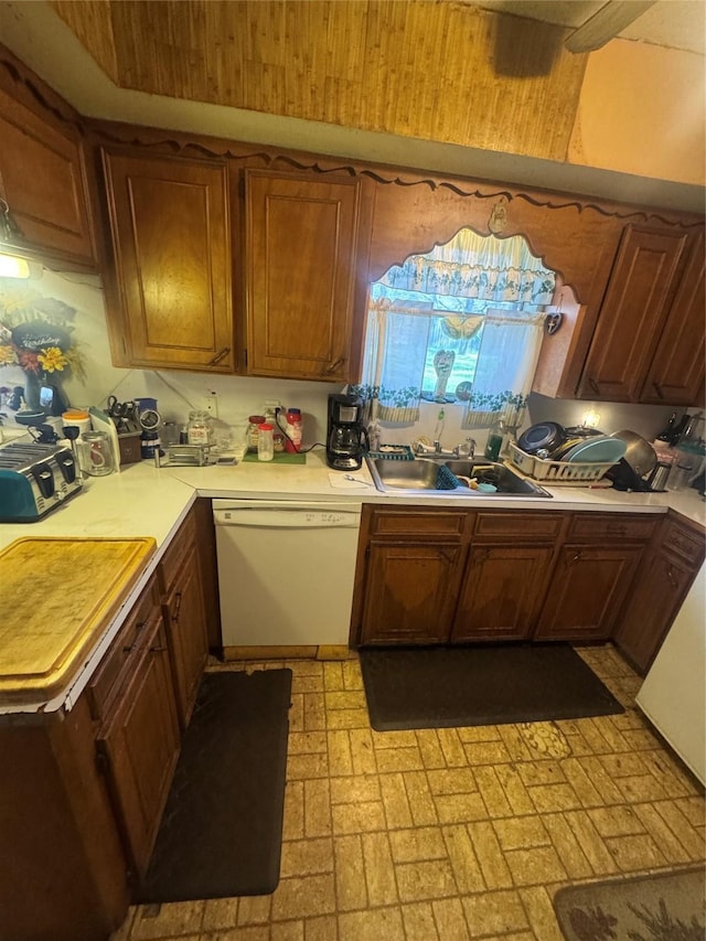 kitchen with brown cabinetry, white dishwasher, a sink, light countertops, and brick patterned floor